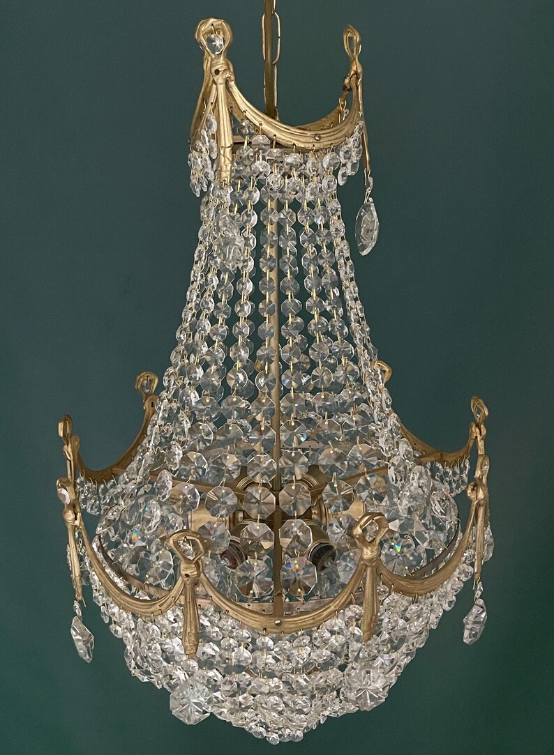 May include: A vintage chandelier with a gold-toned metal frame and cascading crystal beads and pendants. The ornate design features curved arms and decorative accents, creating a luxurious and elegant lighting fixture. The crystals reflect light, adding sparkle.