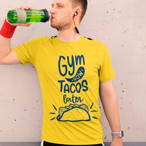 K&ouml;nnte beinhalten: Ein gelbes T-Shirt mit dem Text "Gym Now Tacos Later" in blauer Schrift. Das Shirt zeigt au&szlig;erdem eine Comic-Zeichnung eines Tacos.