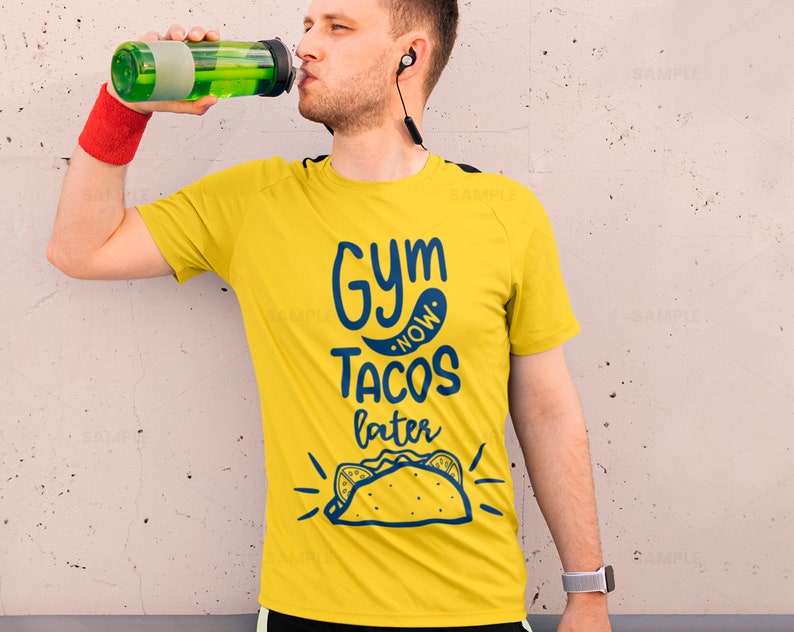 K&ouml;nnte beinhalten: Ein gelbes T-Shirt mit dem Text "Gym Now Tacos Later" in blauer Schrift. Das Shirt zeigt au&szlig;erdem eine Comic-Zeichnung eines Tacos.