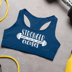 K&ouml;nnte beinhalten: Ein marineblauer Sport-BH mit dem Text "Stronger than my excuses" und einer wei&szlig;en Hantelgrafik.