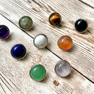 May include: Individual round gemstone cabochons in various colors, including amethyst, lapis lazuli, tiger's eye, black onyx, white howlite, carnelian, rose quartz, and green aventurine. The stones are set in silver-toned bezels. Individual snap buttons fit 12mm snap bases.