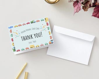 May include: A blue thank you card with a border of colourful toy cars, trucks, and a train. The text on the card reads "Vroom Vroom, Choo Choo, Thank You! Love, Theo."