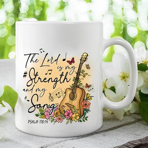 K&ouml;nnte beinhalten: Wei&szlig;e Keramiktasse mit einem farbenfrohen Design mit einer Gitarre, Blumen, Noten und dem Text "The Lord is my Strength and my Song, Psalm 118:14".
