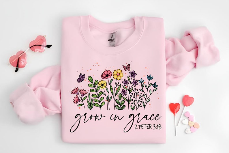 K&ouml;nnte beinhalten: Rosafarbener Pullover mit einem Blumendesign und dem Text "grow in grace 2 Peter 3:18".