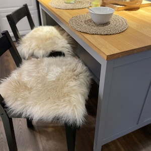 May include: A kitchen island with a light grey painted base and a wood worktop. Two black chairs with faux fur seat cushions are positioned in front of the island. A white bowl and a glass jug are on the worktop.