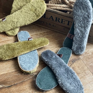 May include: Four pairs of sheepskin insoles, two pairs are green and two pairs are gray. The insoles are laid out on a wooden surface.