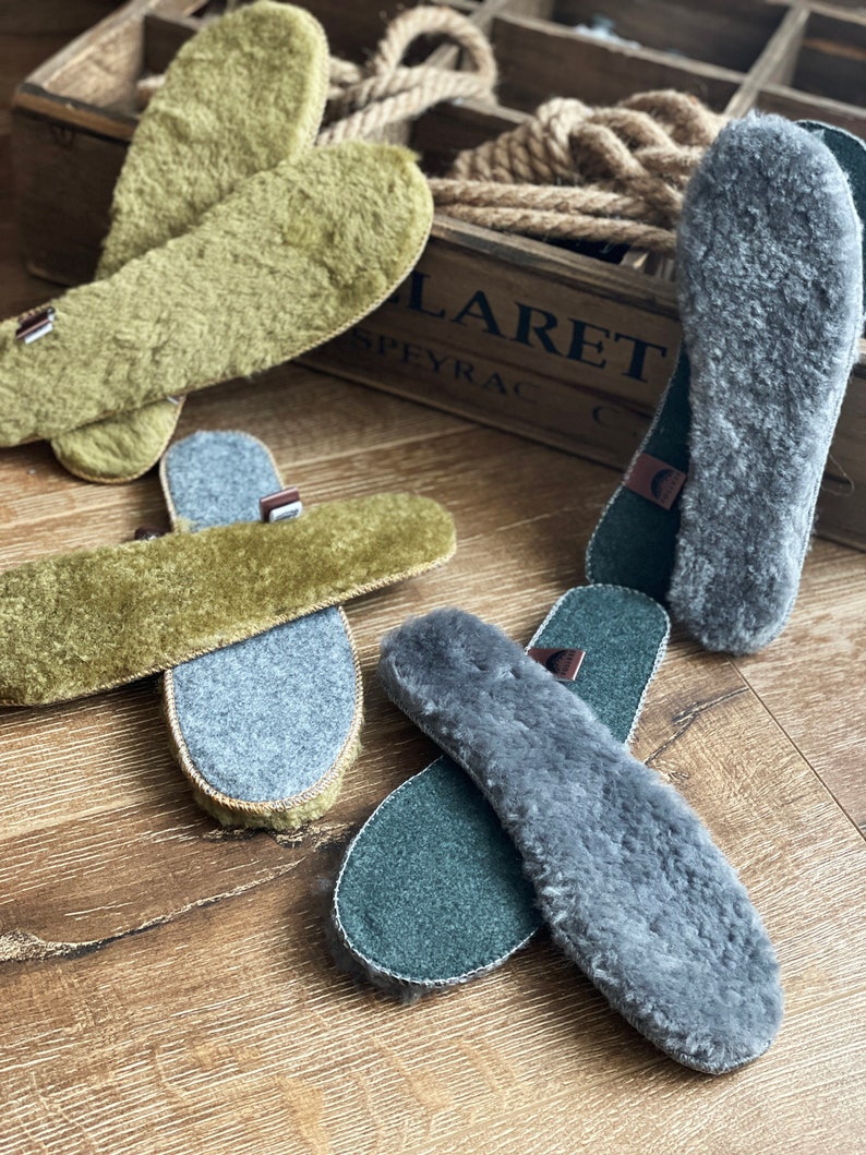 May include: Four pairs of sheepskin insoles, two pairs are green and two pairs are gray. The insoles are laid out on a wooden surface.