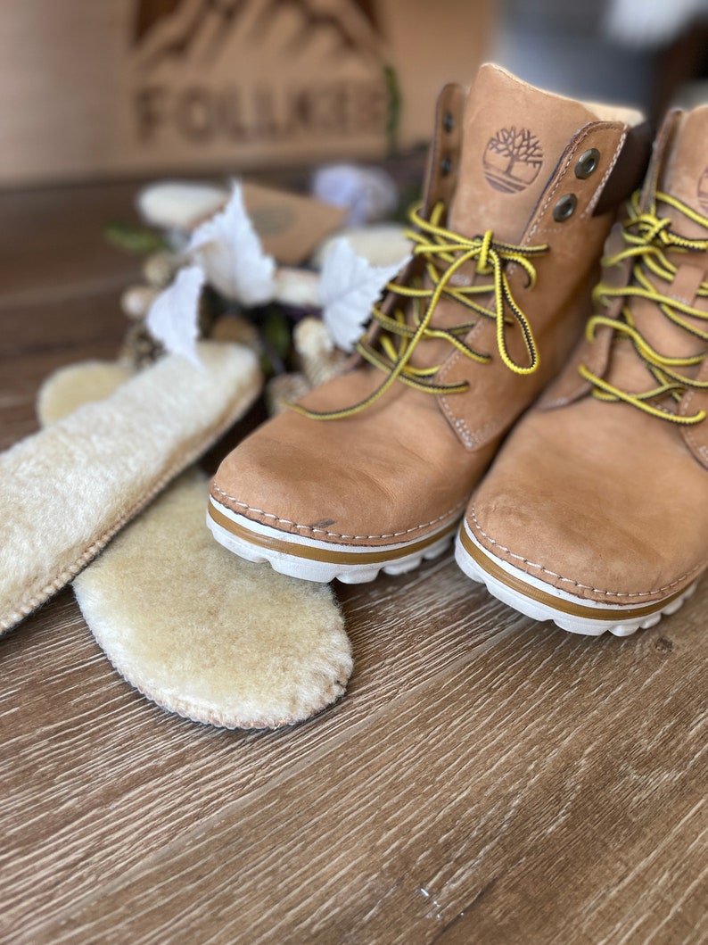 May include: A pair of tan leather boots with yellow laces and a white sole. The boots have a brown leather logo on the side that says "Timberland".