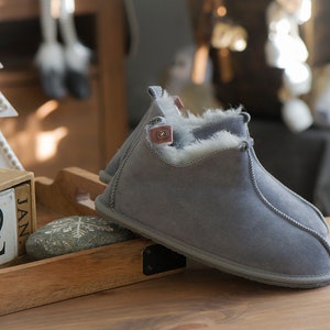 May include: A pair of grey suede slippers with a white faux fur lining. The slippers are on a wooden surface with a calendar that says "Jan 22".
