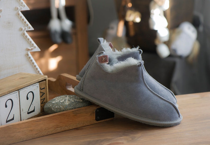 May include: A pair of grey suede slippers with a white faux fur lining. The slippers are on a wooden surface with a calendar that says "Jan 22".