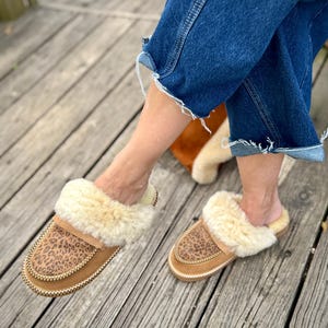 Puede incluir: Zapatillas de ante color canela con diseño de estampado de leopardo en la parte superior y forro de borrego color crema. Las zapatillas tienen un ribete cosido y están diseñadas para uso en interiores.