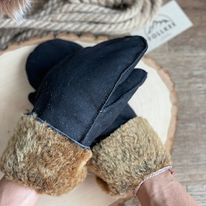 May include: Black leather gloves with brown fur trim. The gloves are on a wooden surface.