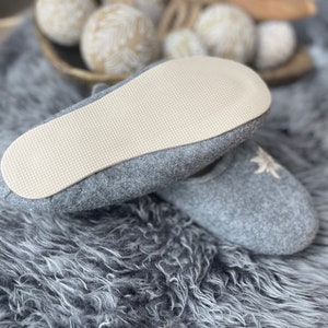 Pode incluir: Chinelos de feltro cinza com um design de flor bordada branca. Os chinelos t&ecirc;m uma sola de borracha branca.