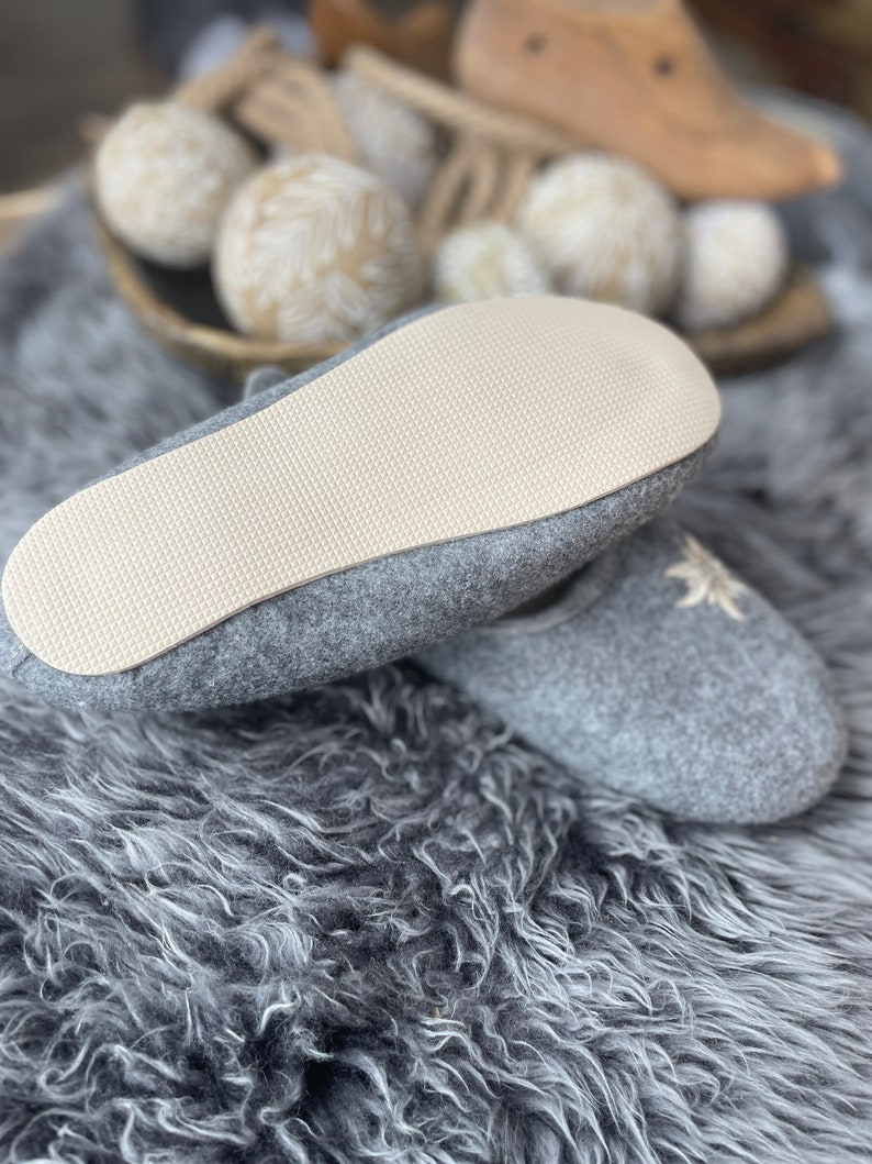 Pode incluir: Chinelos de feltro cinza com um design de flor bordada branca. Os chinelos t&ecirc;m uma sola de borracha branca.