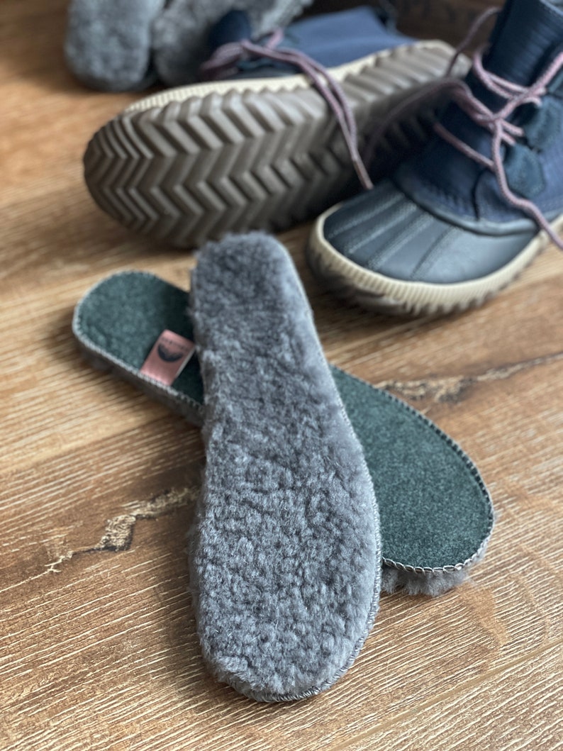 May include: A pair of gray fleece shoe insoles with a black felt backing. The insoles are folded in half and the fleece side is facing the camera.