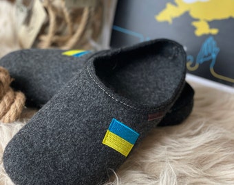 May include: A pair of gray felt slippers with a yellow and blue Ukrainian flag embroidered on the top of one slipper.