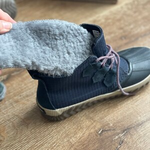 May include: A pair of navy blue winter boots with a gray fleece lining. The boots have a black rubber outsole with a zig-zag pattern.