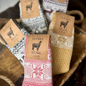 May include: Four pairs of alpaca wool socks with a snowflake pattern. The socks are in different colors: gray, red, yellow, and brown. Each sock has a tag with the words "Alpaca Wool" and the size.