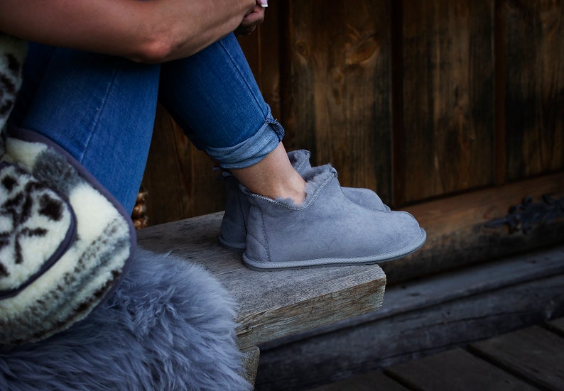 May include: Grey suede ankle boots with a soft, fluffy lining. The boots are being worn by a person sitting on a wooden bench.