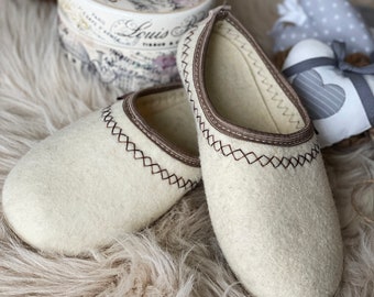 May include: A pair of off-white wool slippers with brown stitching around the top edge. The slippers are on a fluffy, light brown rug.