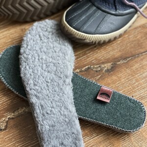 May include: A pair of gray fleece insoles with a green felt insole with the word "Follea" on a brown leather tag.