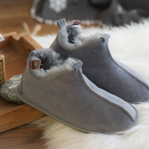 May include: A pair of grey suede slippers with a fluffy white lining. The slippers have a simple design and are perfect for keeping your feet warm in the winter.