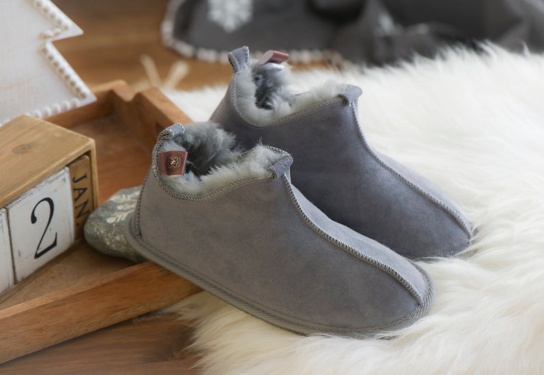 May include: A pair of grey suede slippers with a fluffy white lining. The slippers have a simple design and are perfect for keeping your feet warm in the winter.