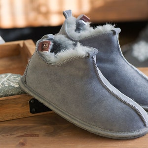 May include: A pair of grey suede slippers with a white fur lining. The slippers have a rounded toe and a low heel.