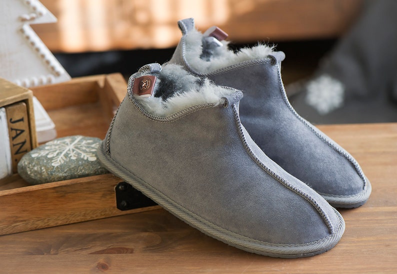 May include: A pair of grey suede slippers with a white fur lining. The slippers have a rounded toe and a low heel.