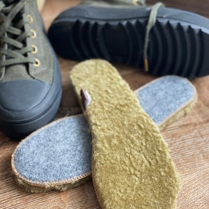 May include: Two pairs of green fleece shoe insoles. One pair is gray on the bottom and the other pair is green on the bottom. The insoles are on a wooden surface.