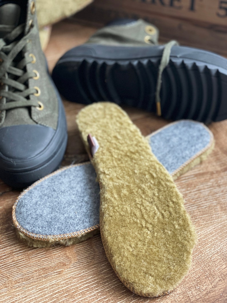 May include: Two pairs of green fleece shoe insoles. One pair is gray on the bottom and the other pair is green on the bottom. The insoles are on a wooden surface.