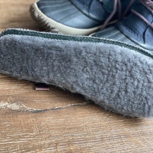 May include: Close-up of the gray fleece lining inside a pair of dark blue winter boots.