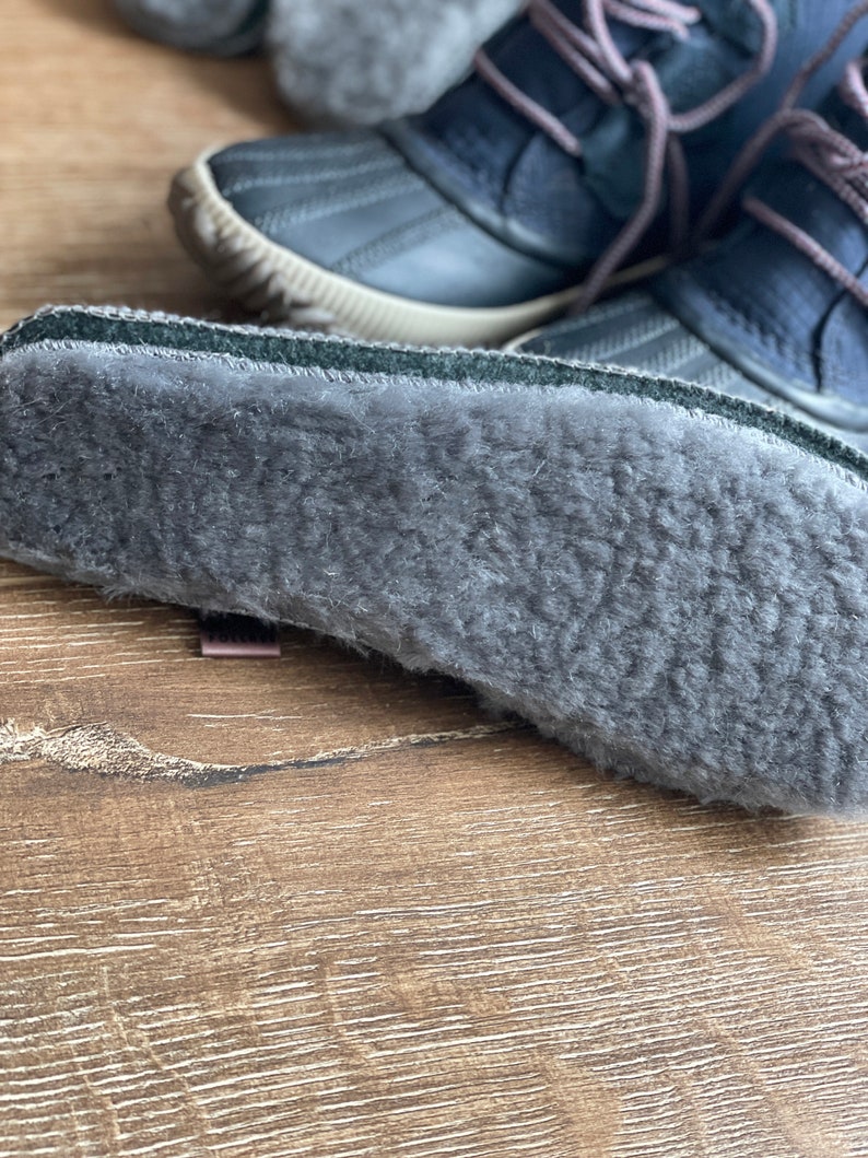 May include: Close-up of the gray fleece lining inside a pair of dark blue winter boots.