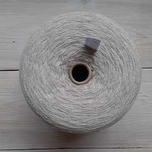 May include: A large ball of beige yarn, wound into a circular shape. The yarn is made from natural fibres and has a soft, textured look.