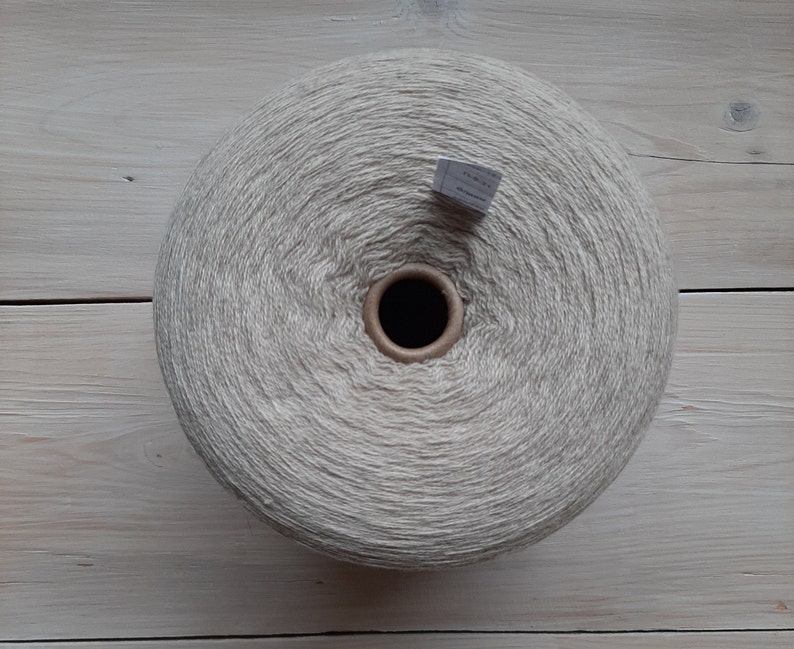 May include: A large ball of beige yarn, wound into a circular shape. The yarn is made from natural fibres and has a soft, textured look.