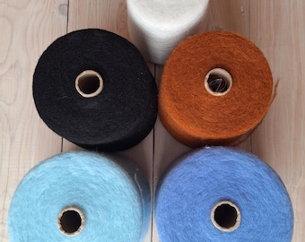 May include: Five spools of yarn in different colours: black, white, light blue, dark blue, and orange. The spools are arranged in a circle on a wooden surface.