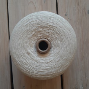 May include: A ball of white yarn wound on a cardboard spool. The yarn is soft and fluffy, and the spool is brown.