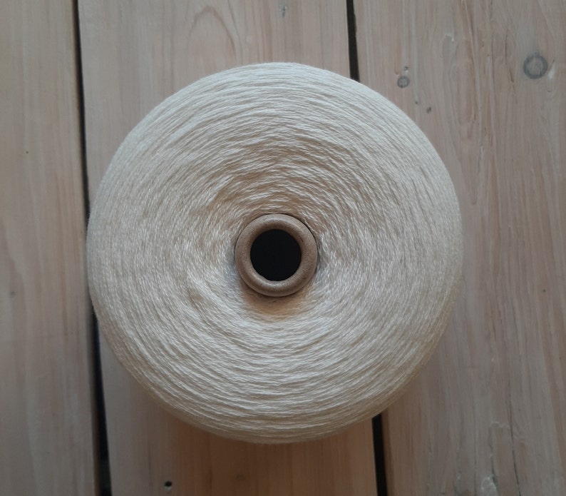 May include: A ball of white yarn wound on a cardboard spool. The yarn is soft and fluffy, and the spool is brown.