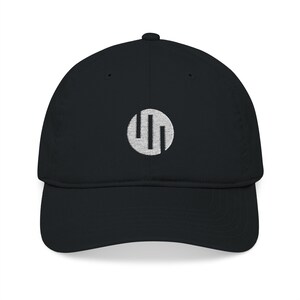 May include: Black baseball cap with a curved peak. The cap has a white circular emblem with two vertical lines inside. The hat is made of a soft material and has a classic, casual style.