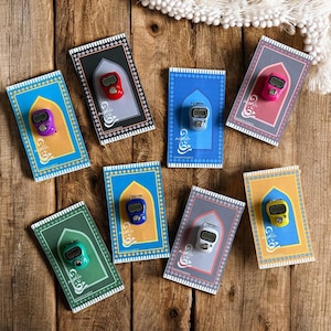 May include: Assortment of colorful prayer rugs with digital tasbihs, or prayer beads, on top. The rugs are decorated with Islamic calligraphy and geometric patterns. The tasbihs are in various colors, including blue, green, red, yellow, and white.