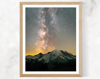 May include: A framed photograph of a mountain range with the Milky Way galaxy visible in the night sky. The mountain peaks are covered in snow and the sky is filled with stars.