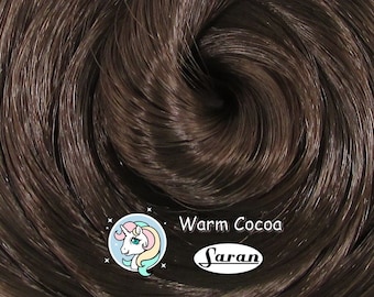 May include: Close-up of a spool of warm cocoa brown saran hair. The hair is soft and shiny, and it is perfect for making wigs, dolls, and other crafts.