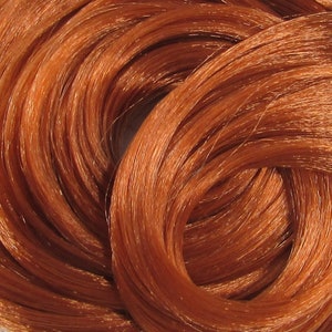 May include: Close-up of a bundle of long, bright copper-colored hair. The strands are tightly woven together, creating a smooth, shiny surface.