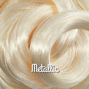 May include: Close-up of a bundle of shiny, pale gold metallic thread. The strands are tightly curled, creating a textured, reflective surface. The word "Metallic" is written in a white, cursive font.