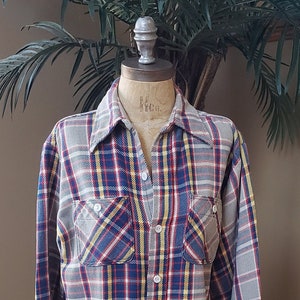 May include: A long-sleeved plaid shirt with a blue, red, yellow, and white plaid pattern. The shirt has a button-down collar and two chest pockets.