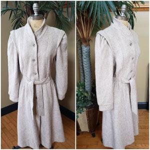 May include: A long-sleeved, beige wool coat with a button-up front, a belt, and a slightly flared skirt. The coat has a high collar and puffed shoulders.