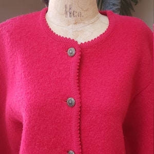 May include: A red cardigan sweater with a scalloped neckline and five gold buttons. The cardigan is made of a soft, fuzzy material.