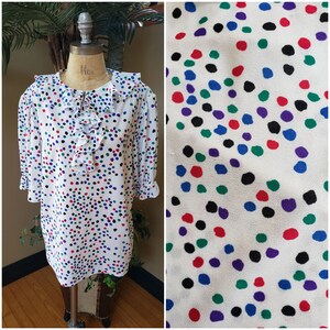 May include: A white blouse with a ruffled collar and a colorful polka dot pattern. The dots are red, blue, green, purple, and black.