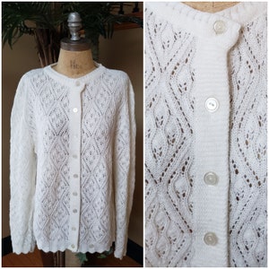 May include: White crocheted cardigan with a button-up front and a diamond pattern. The cardigan has a scalloped hem.
