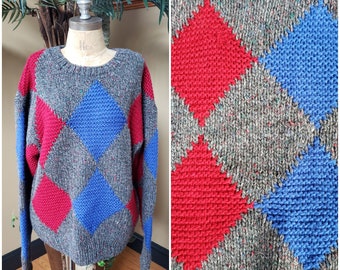 Puede incluir: Un suéter de punto gris, rojo y azul con estampado de rombos. El suéter tiene cuello redondo y mangas largas.